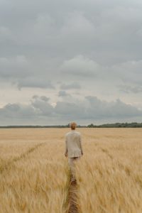 back view of a person in beige suit standing on brown grass field under the sky